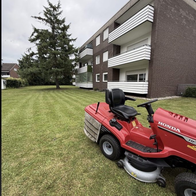 Grünanlagenpflege | Rasenmähen | Unkrautbeseitigung | Pflasterarbeiten | Laubbeseitigung | Heckenschnitt Grünes, frisch gemähtes Gelände mit einem Baum und Wohngebäuden im Hintergrund.